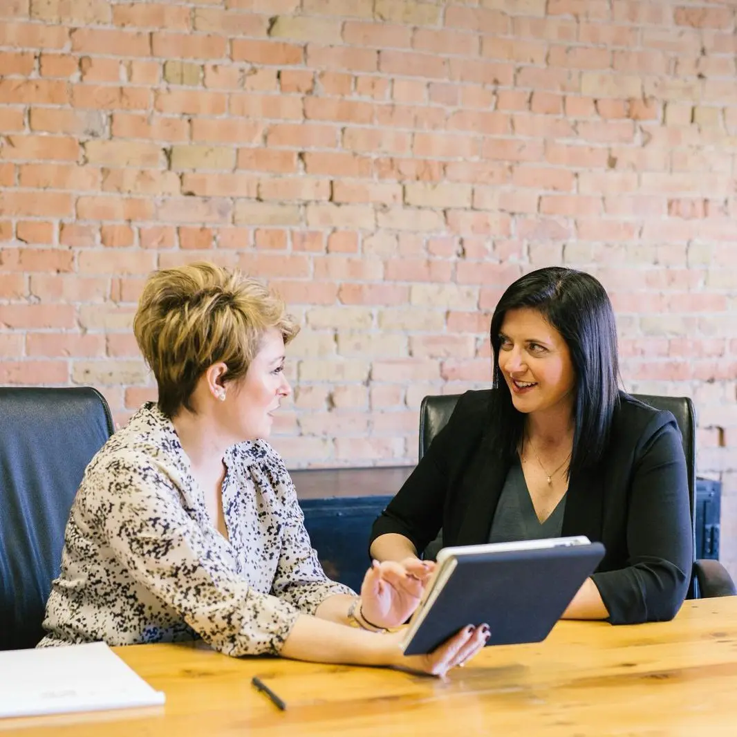Deux femmes discutant avec tablette en réunion.