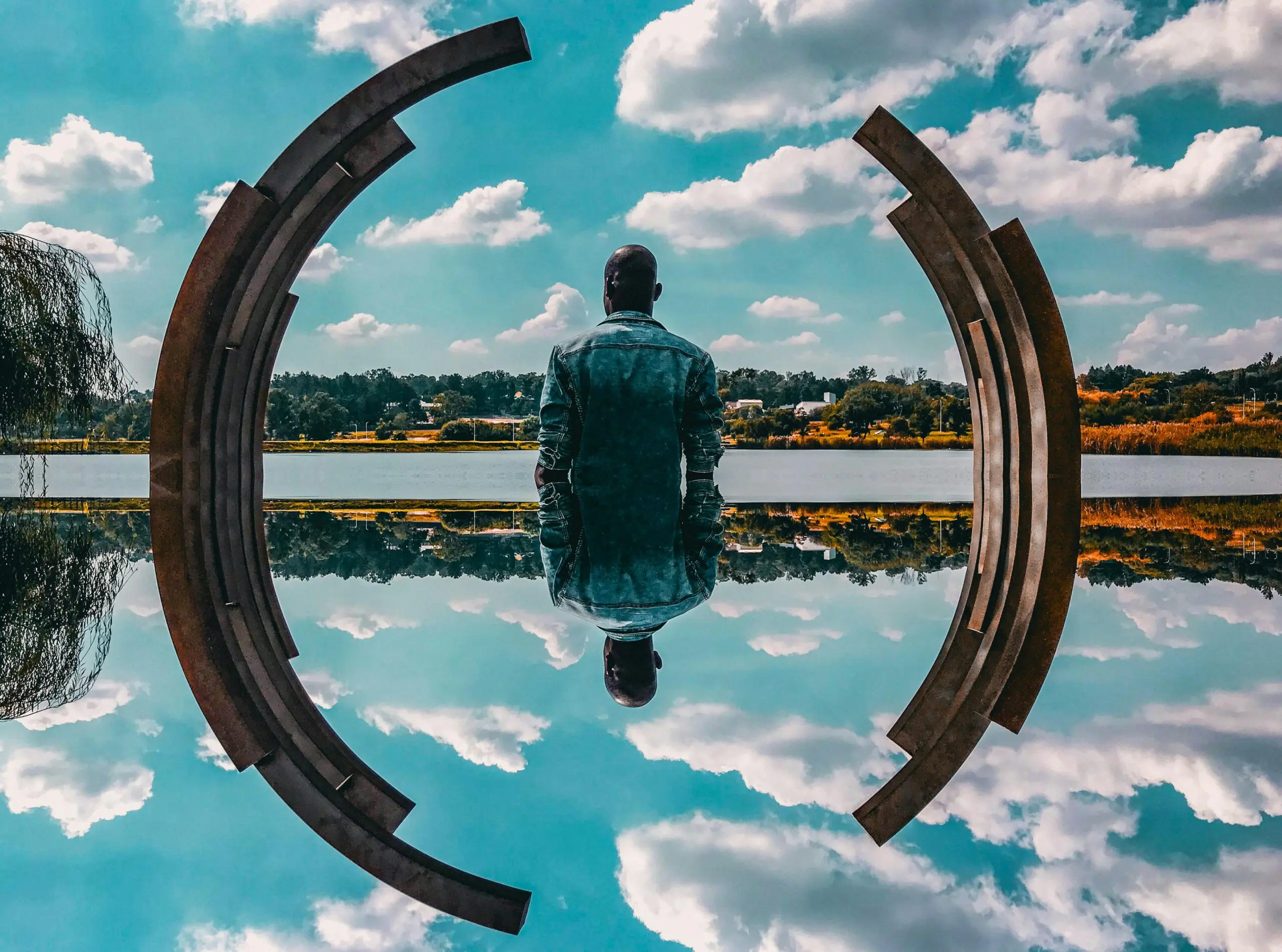 Homme assis devant lac, entouré de sculptures métalliques.